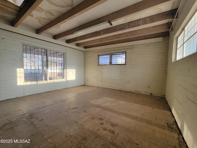 empty room with brick wall, a healthy amount of sunlight, and beam ceiling