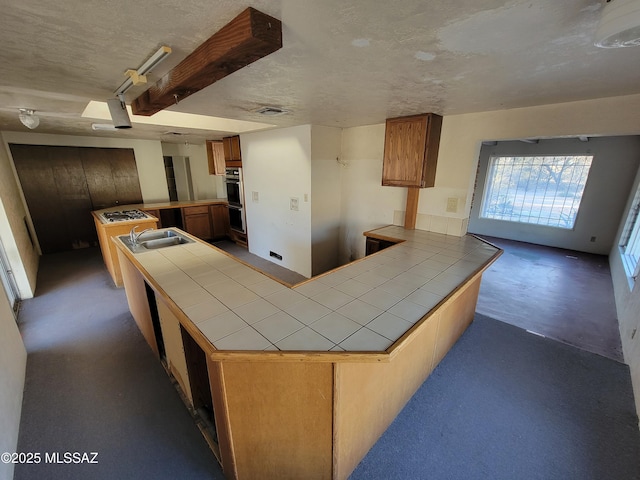 kitchen featuring tile countertops, stainless steel gas stovetop, sink, black double oven, and kitchen peninsula