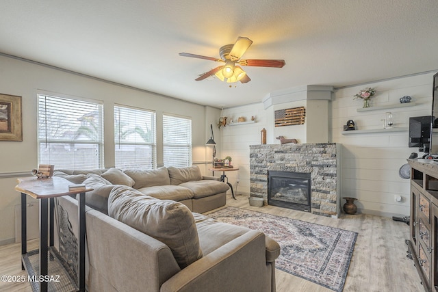 living room with ceiling fan, a textured ceiling, a fireplace, and light hardwood / wood-style flooring