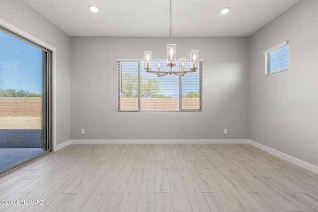 empty room with an inviting chandelier, a healthy amount of sunlight, and light hardwood / wood-style floors