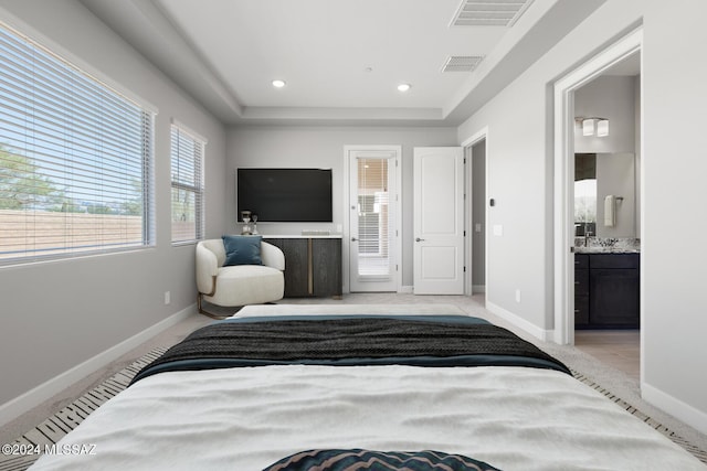 bedroom featuring a raised ceiling, light colored carpet, and ensuite bath