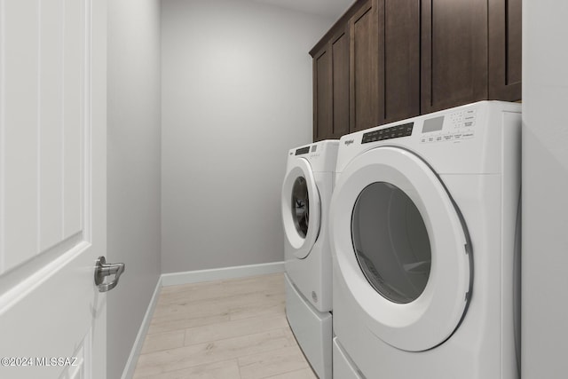 laundry room featuring cabinets, washing machine and dryer, and light hardwood / wood-style flooring