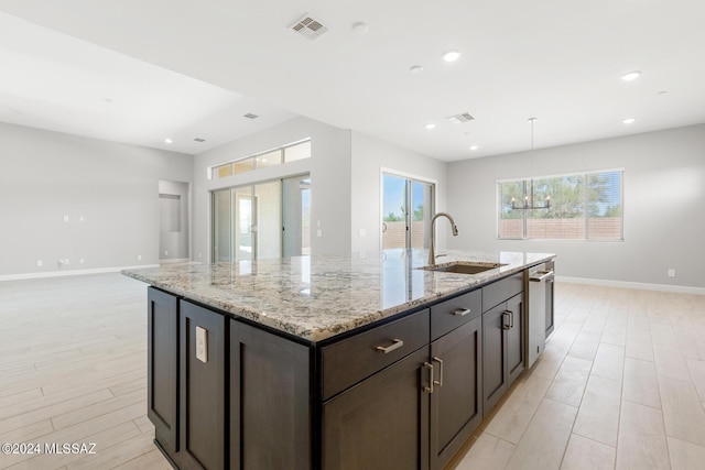 kitchen with light stone counters, a kitchen island with sink, sink, and dark brown cabinets