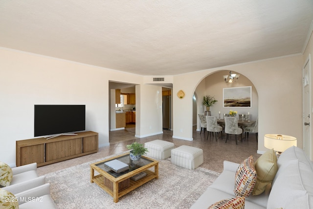 living room featuring arched walkways, baseboards, an inviting chandelier, visible vents, and ornamental molding