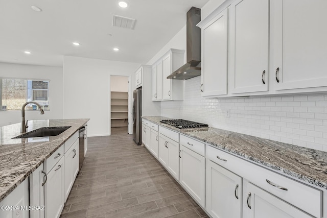 kitchen featuring wall chimney range hood, sink, stainless steel appliances, light stone counters, and white cabinets