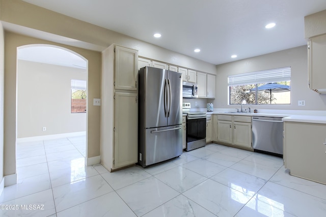 kitchen with a sink, recessed lighting, stainless steel appliances, arched walkways, and light countertops