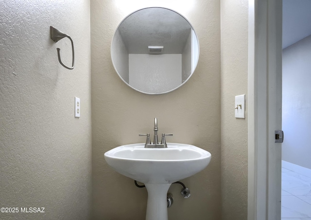 bathroom featuring marble finish floor and a textured wall