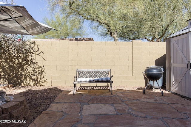 view of patio featuring a storage unit, area for grilling, an outdoor structure, and a fenced backyard