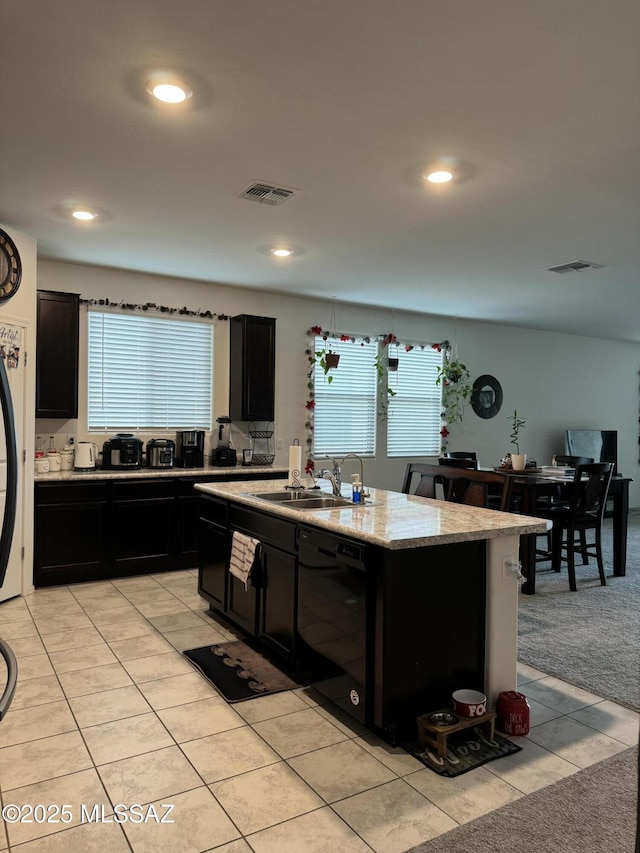 kitchen featuring sink, light tile patterned floors, dishwasher, light stone counters, and a center island with sink