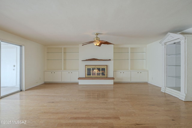 unfurnished living room featuring built in shelves, a glass covered fireplace, and light wood-style flooring