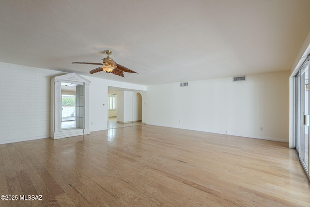 unfurnished room with arched walkways, light wood-type flooring, visible vents, and a ceiling fan