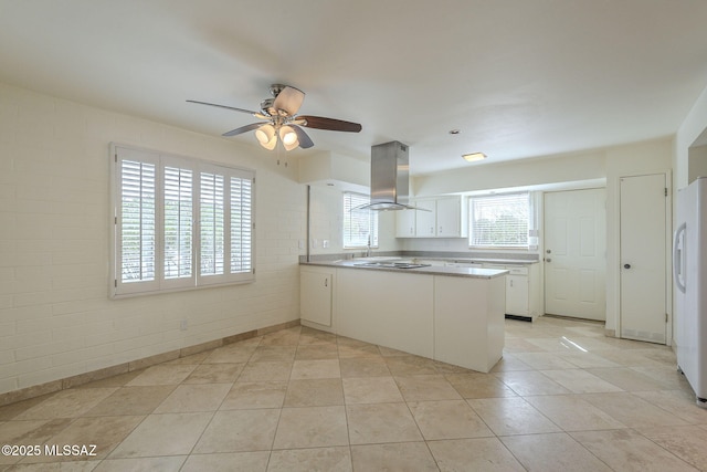 kitchen featuring island exhaust hood, freestanding refrigerator, white cabinets, brick wall, and a peninsula