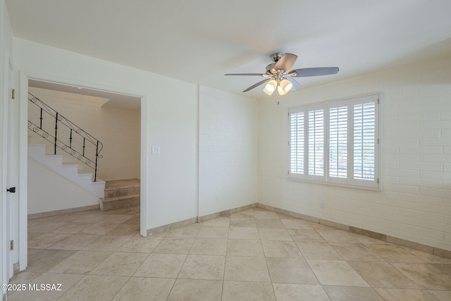 empty room featuring a ceiling fan, stairway, brick wall, and light tile patterned floors