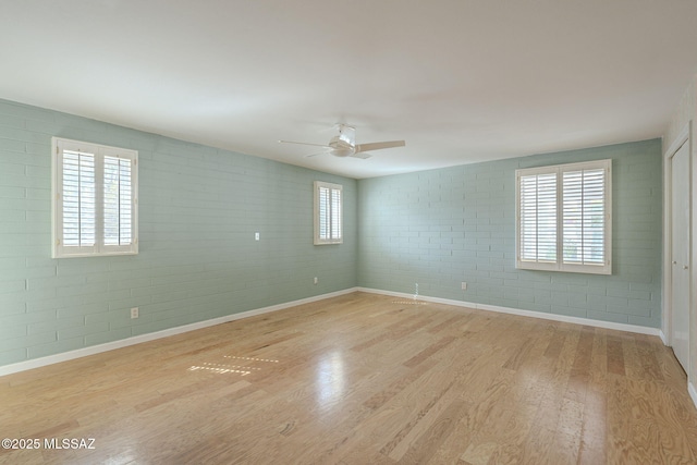 unfurnished room featuring a ceiling fan, light wood-type flooring, brick wall, and baseboards