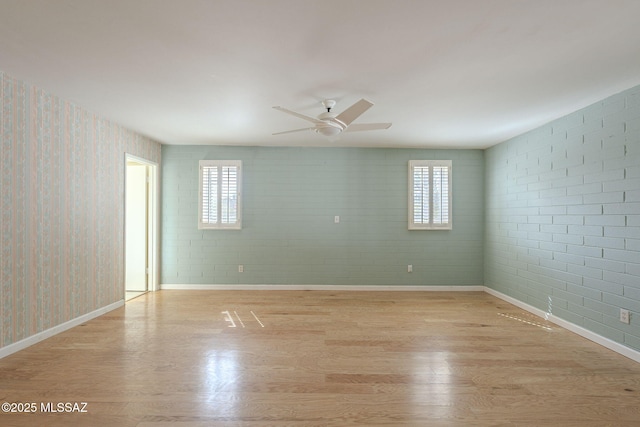 empty room featuring light wood-type flooring, wallpapered walls, ceiling fan, and baseboards