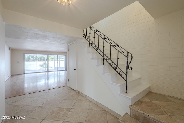 stairway with brick wall and tile patterned floors