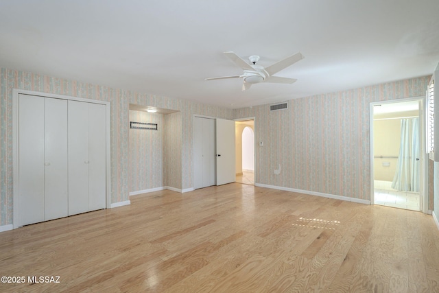 unfurnished bedroom featuring wallpapered walls, visible vents, arched walkways, wood finished floors, and two closets