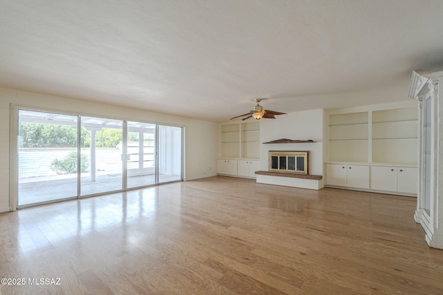 unfurnished living room featuring light wood finished floors, a glass covered fireplace, and a ceiling fan