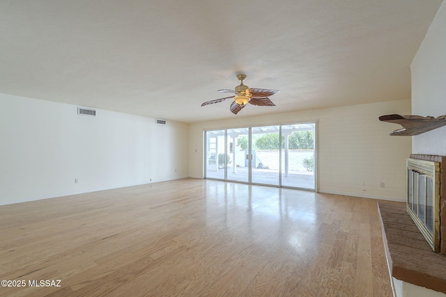 unfurnished living room with light wood-style flooring, a fireplace, visible vents, and ceiling fan