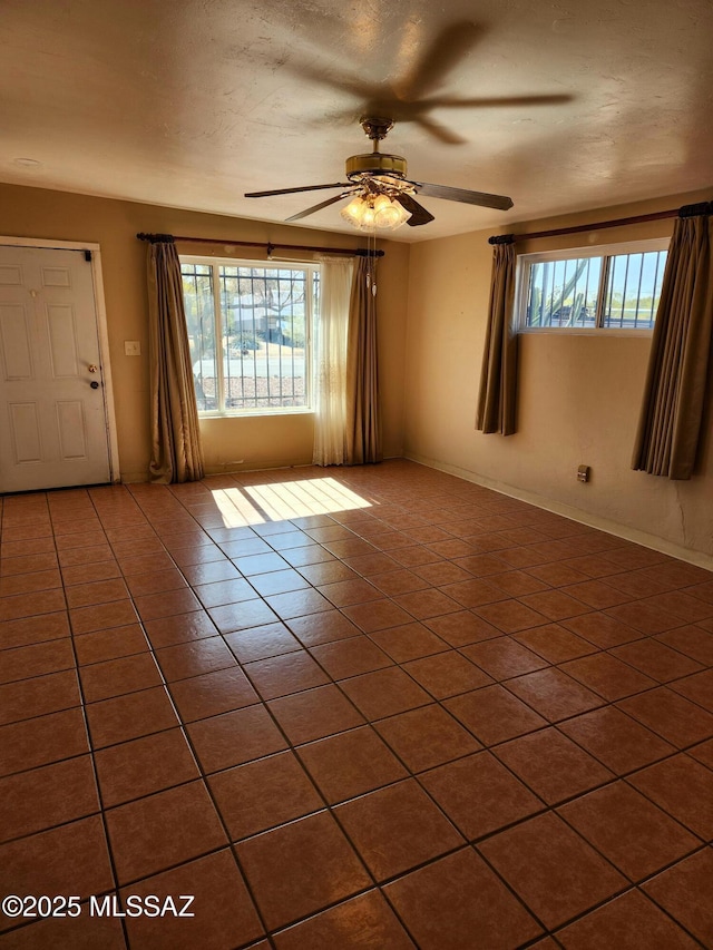 empty room with plenty of natural light, tile patterned floors, and ceiling fan