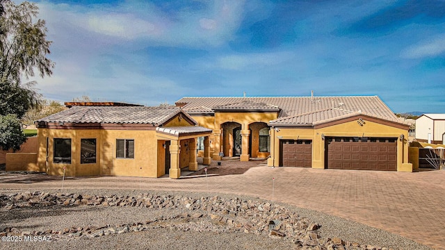 mediterranean / spanish-style home with an attached garage, stucco siding, decorative driveway, and a tiled roof