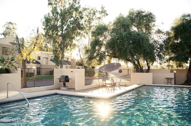 pool with a patio area, fence, and grilling area