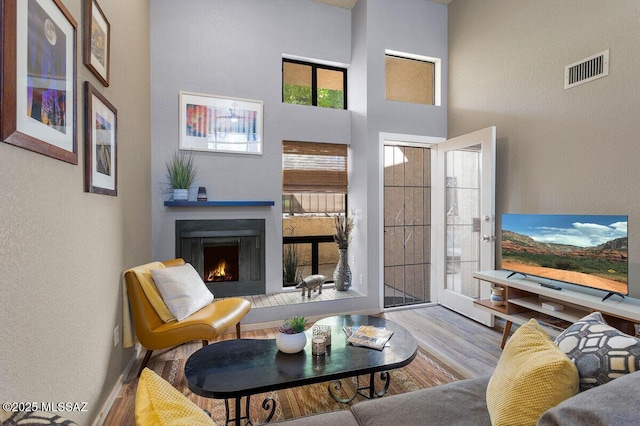 living room with visible vents, a lit fireplace, a towering ceiling, and wood finished floors