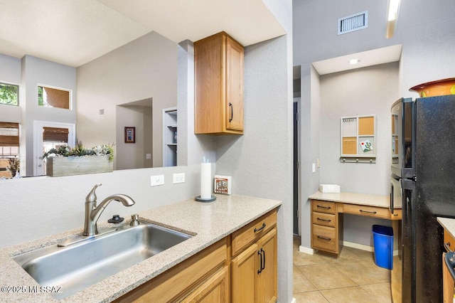 kitchen featuring light tile patterned floors, a sink, visible vents, freestanding refrigerator, and light stone countertops