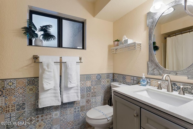 bathroom featuring toilet, a wainscoted wall, vanity, and tile walls