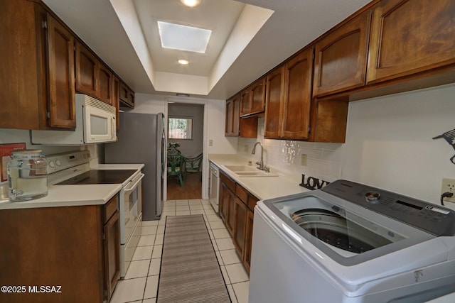 kitchen with sink, a skylight, a tray ceiling, white appliances, and washer / clothes dryer