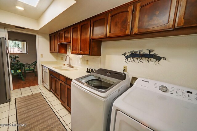 washroom with sink, light tile patterned floors, a skylight, cabinets, and independent washer and dryer