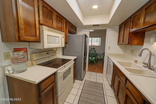 kitchen featuring sink, white appliances, light tile patterned floors, tasteful backsplash, and a raised ceiling