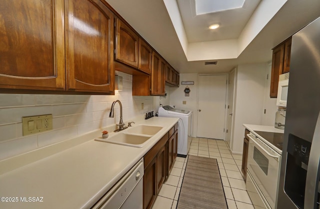 kitchen featuring tasteful backsplash, sink, washing machine and clothes dryer, a raised ceiling, and white appliances