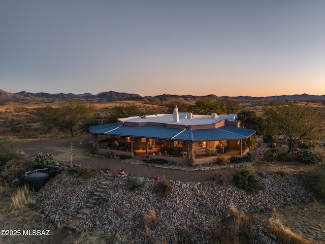 back of house at dusk with a chimney, a patio area, and a mountain view