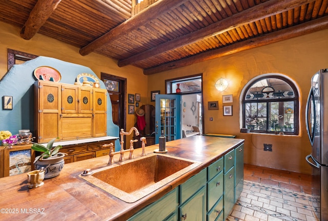 kitchen featuring wood ceiling, beamed ceiling, freestanding refrigerator, brick floor, and a sink