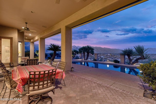 patio terrace at dusk featuring an outdoor pool, a mountain view, outdoor dining area, and a ceiling fan