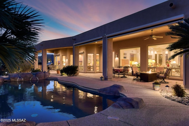 pool at dusk featuring a patio area, an outdoor fire pit, an outdoor pool, and a ceiling fan