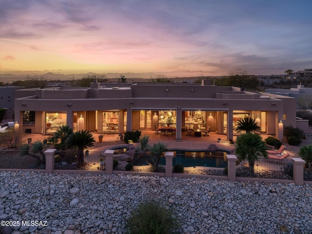 back of property at dusk featuring stucco siding, a fenced front yard, a fenced in pool, and a patio