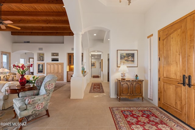 foyer entrance with arched walkways, light tile patterned floors, wood ceiling, a towering ceiling, and ornate columns