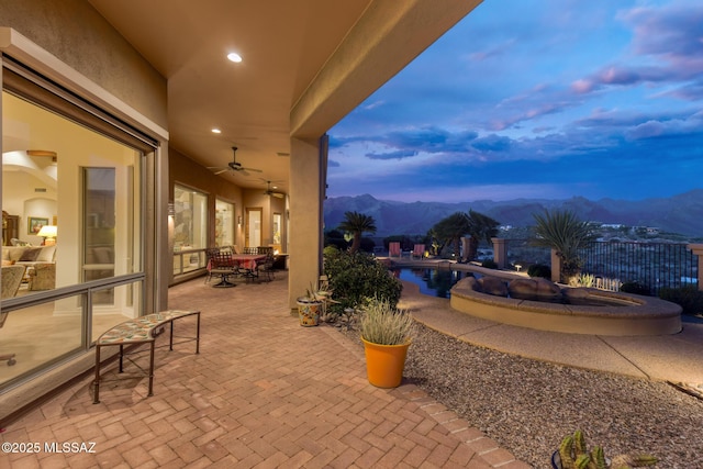 patio terrace at dusk featuring fence, a mountain view, and a ceiling fan