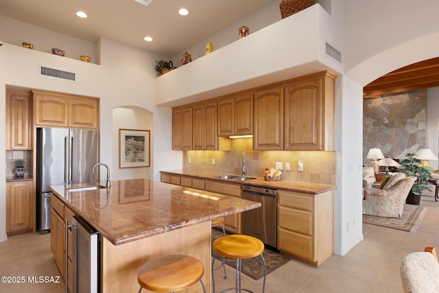 kitchen with visible vents, wine cooler, appliances with stainless steel finishes, a kitchen island with sink, and a sink