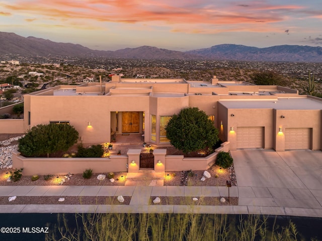 pueblo-style house featuring concrete driveway, a mountain view, a chimney, and stucco siding