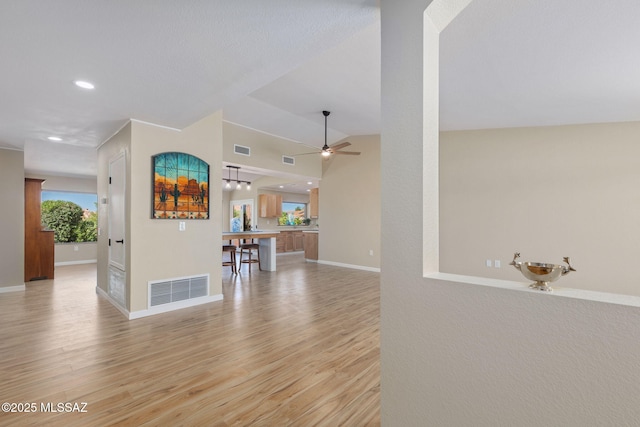 interior space featuring light wood-type flooring, baseboards, visible vents, and vaulted ceiling