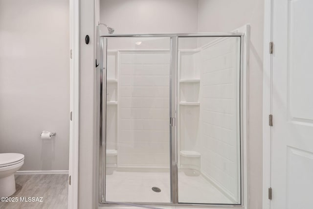 bathroom with toilet, a shower stall, baseboards, and wood finished floors