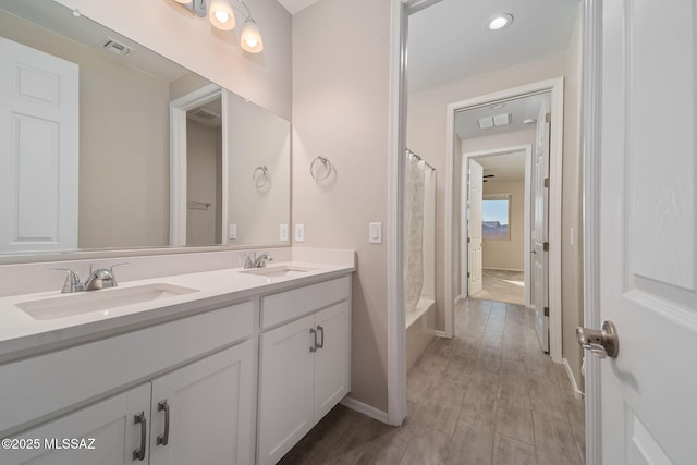 full bath with double vanity, visible vents, a sink, and wood finished floors