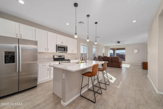 kitchen with a sink, open floor plan, light countertops, appliances with stainless steel finishes, and a center island with sink