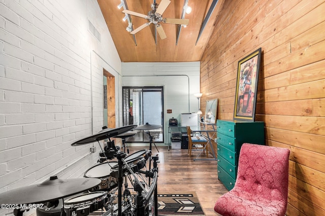 interior space with vaulted ceiling, brick wall, wooden walls, hardwood / wood-style flooring, and ceiling fan