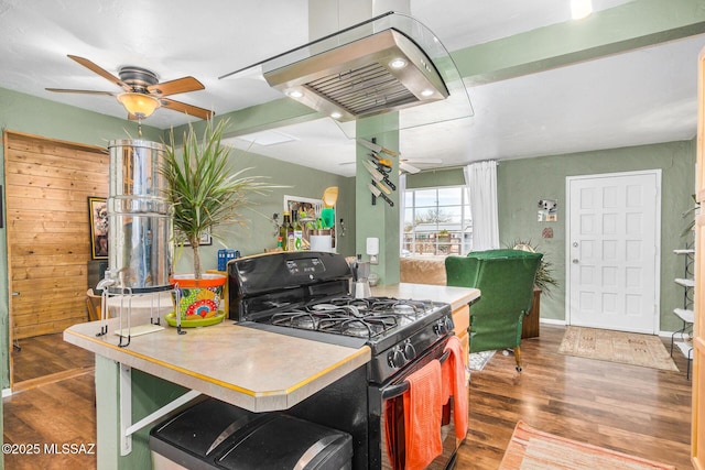 kitchen featuring dark wood-type flooring, ceiling fan, island exhaust hood, a kitchen bar, and black range with gas stovetop