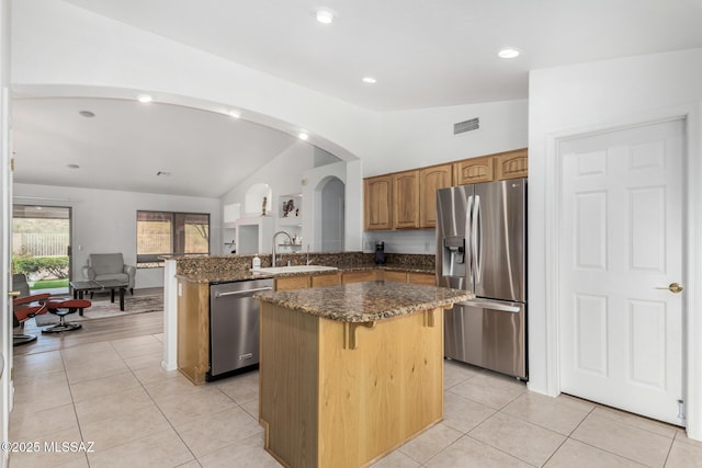 kitchen with light tile patterned floors, appliances with stainless steel finishes, a center island, vaulted ceiling, and kitchen peninsula