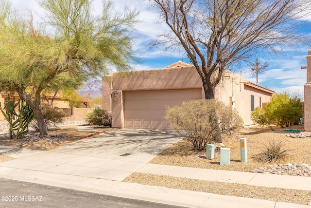 pueblo-style house featuring a garage, concrete driveway, and stucco siding